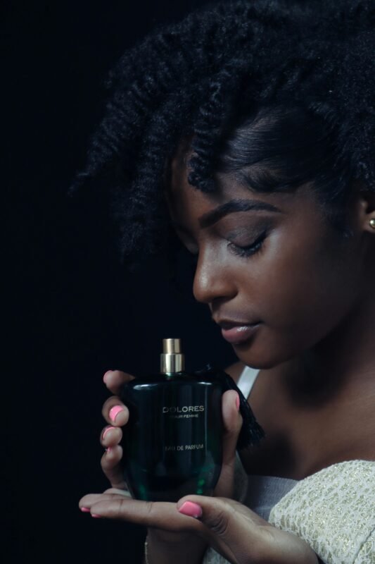 Side view of a woman admiring a perfume bottle with closed eyes, highlighting natural afro hair.